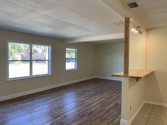 unfurnished room featuring dark wood-style floors, a textured ceiling, visible vents, and baseboards