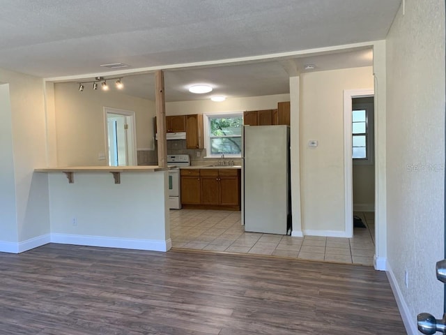 kitchen with brown cabinets, white range with electric cooktop, light countertops, freestanding refrigerator, and a peninsula