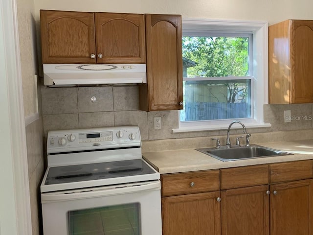 kitchen with white electric stove, backsplash, light countertops, under cabinet range hood, and a sink