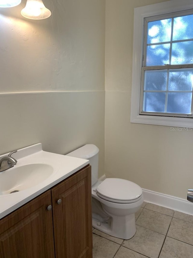 half bath featuring toilet, tile patterned flooring, vanity, and baseboards