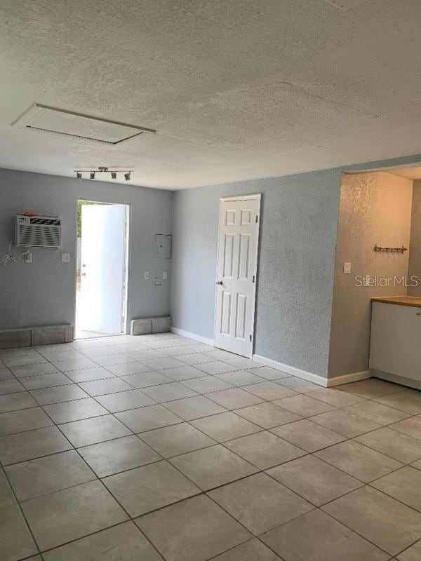 unfurnished room with a wall unit AC, a textured ceiling, baseboards, and light tile patterned floors