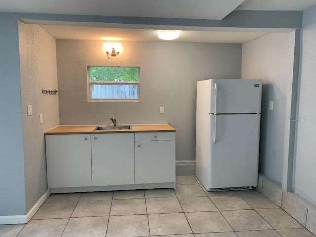 kitchen featuring white cabinets, freestanding refrigerator, light countertops, a sink, and light tile patterned flooring