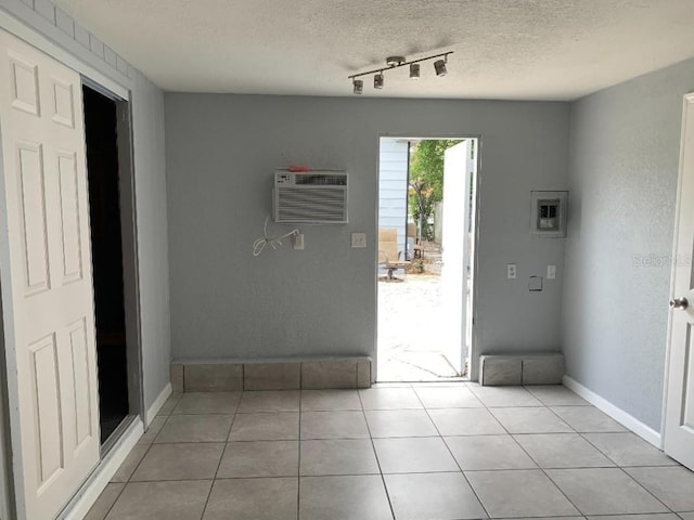 interior space with an AC wall unit, a textured ceiling, baseboards, and light tile patterned floors