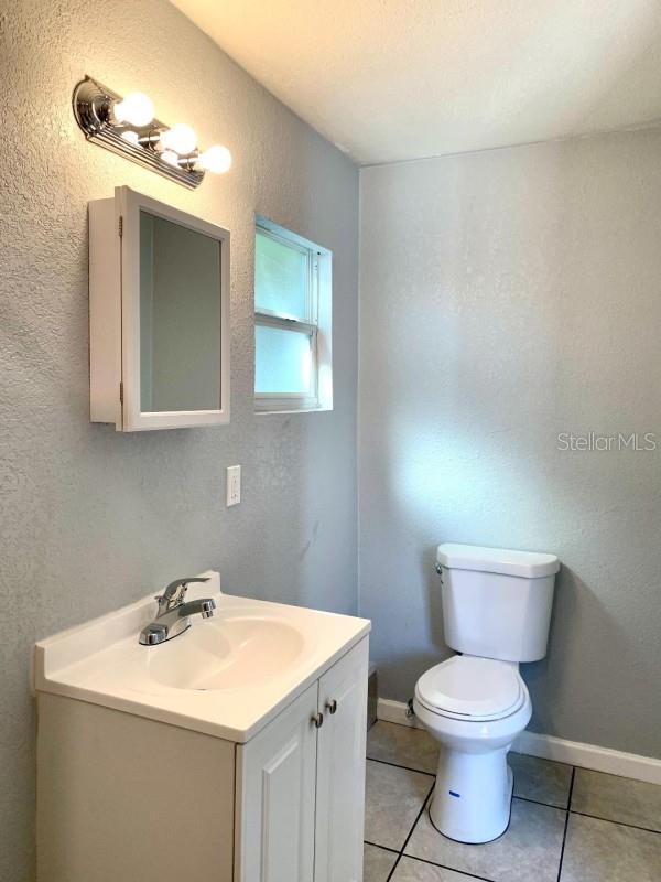 half bathroom with a textured wall, toilet, vanity, baseboards, and tile patterned floors