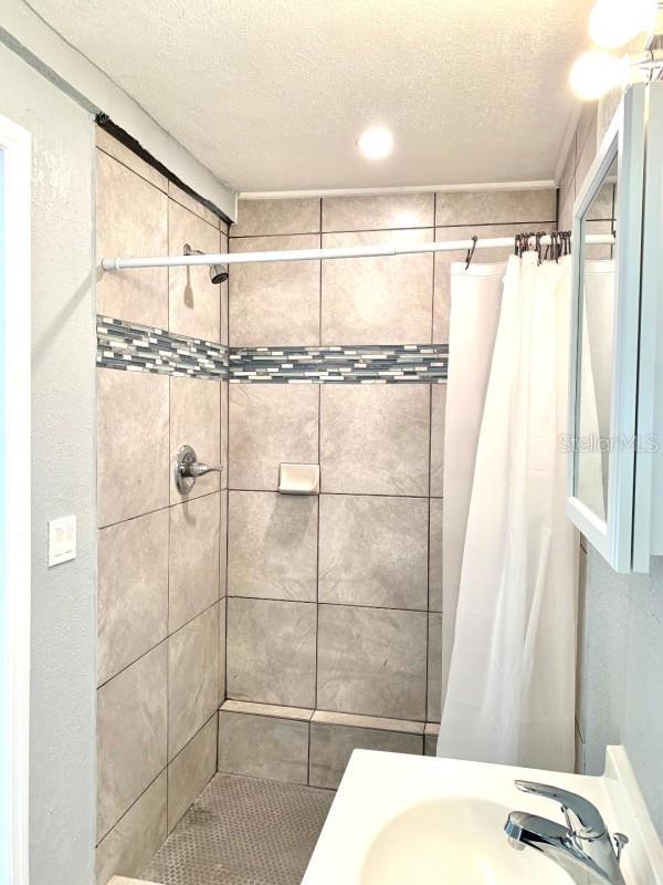 bathroom featuring a textured ceiling, a stall shower, and a sink