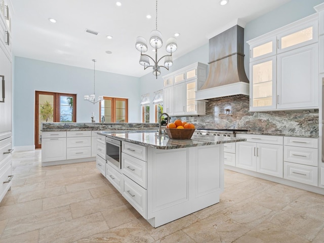 kitchen with an inviting chandelier, white cabinetry, custom exhaust hood, and decorative backsplash