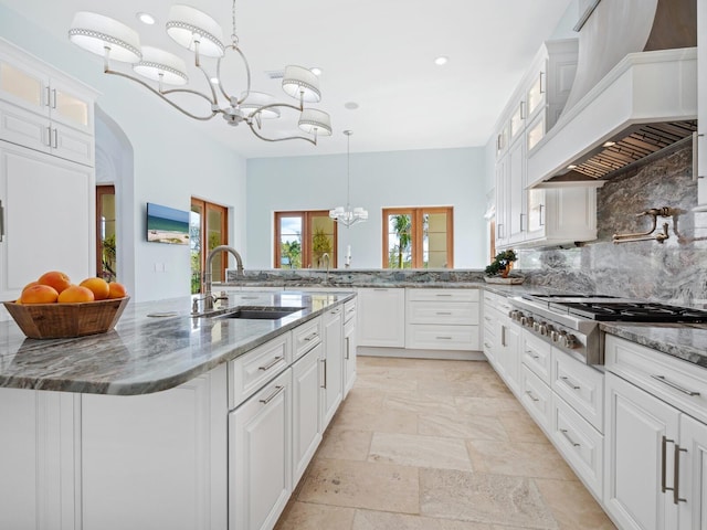 kitchen featuring stainless steel gas cooktop, tasteful backsplash, a sink, a chandelier, and premium range hood