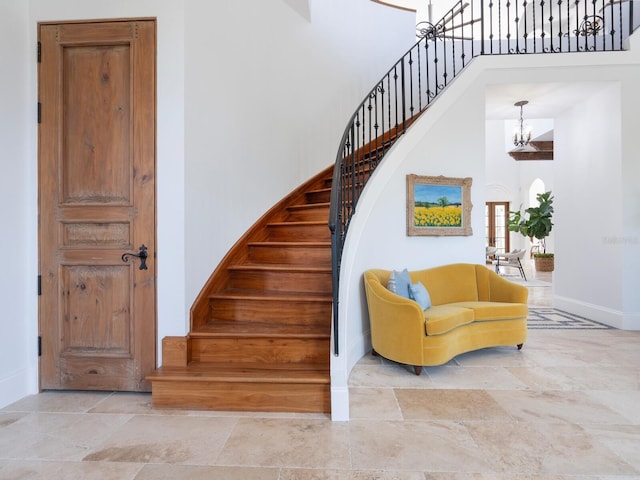 stairs featuring a notable chandelier, a high ceiling, stone finish floor, and baseboards