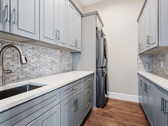 kitchen featuring dark wood-style floors, gray cabinets, light countertops, stacked washing maching and dryer, and a sink