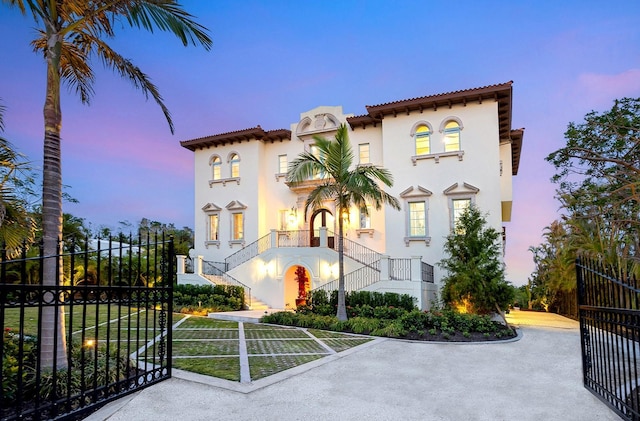 mediterranean / spanish-style home with a fenced front yard, a tiled roof, stairway, a gate, and stucco siding