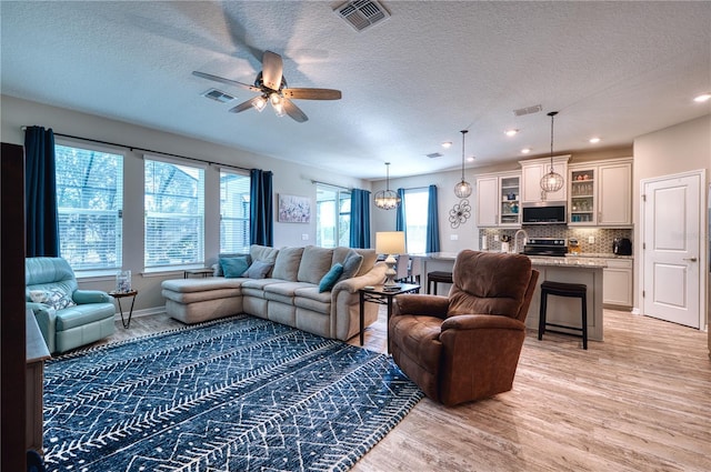 living area featuring light wood-style floors, visible vents, and ceiling fan with notable chandelier