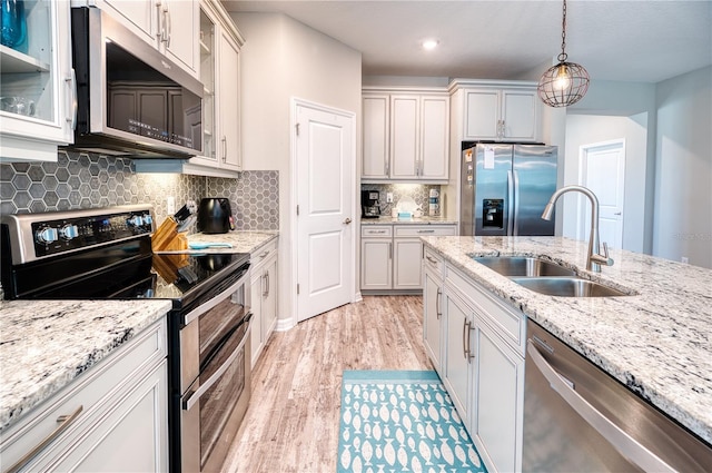 kitchen featuring a sink, hanging light fixtures, appliances with stainless steel finishes, light wood finished floors, and glass insert cabinets