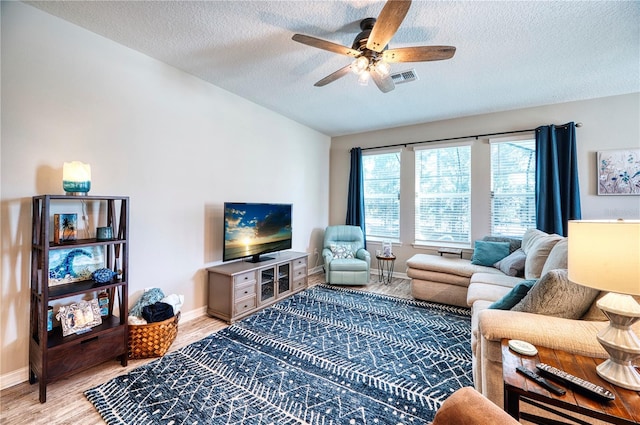 living area with light wood finished floors, lofted ceiling, visible vents, a ceiling fan, and baseboards