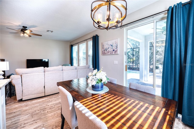 dining space featuring light wood-type flooring, visible vents, a textured ceiling, and ceiling fan with notable chandelier