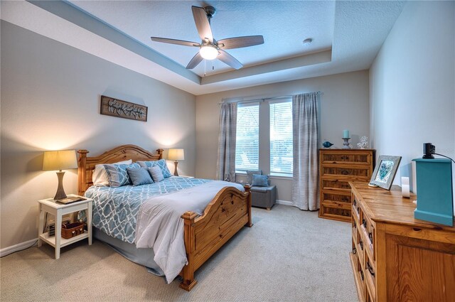 bedroom with baseboards, a textured ceiling, a raised ceiling, and light colored carpet