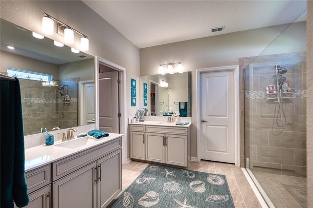 full bathroom featuring visible vents, two vanities, a sink, and tiled shower