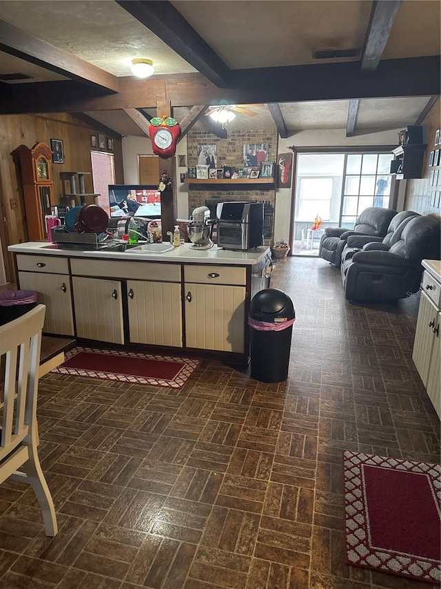 kitchen featuring brick patterned floor, beam ceiling, wood walls, and light countertops