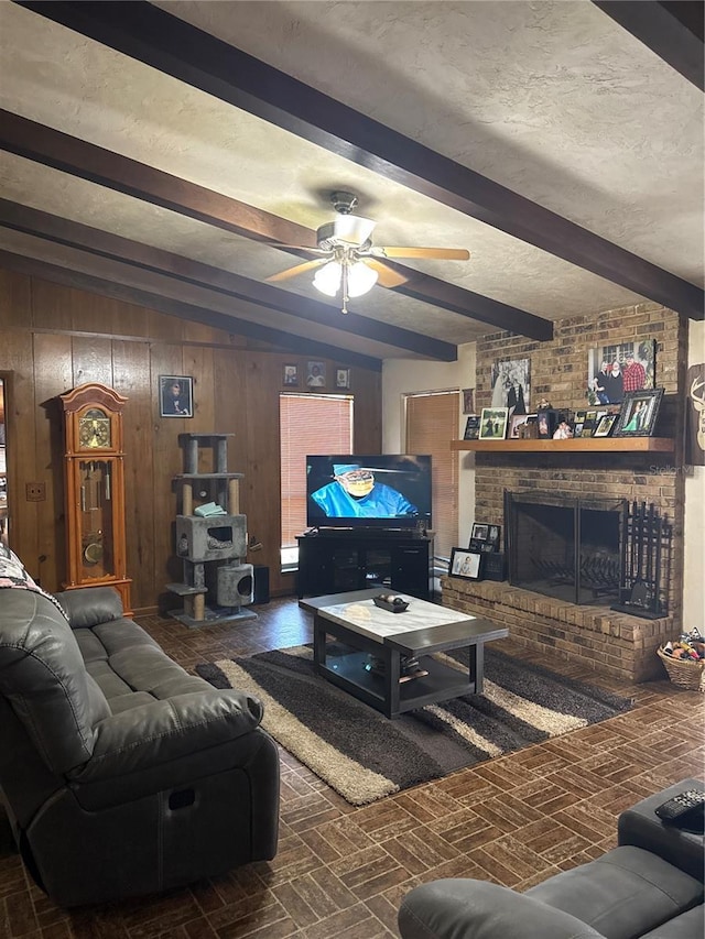 living area with beam ceiling, a textured ceiling, wood walls, brick floor, and a brick fireplace