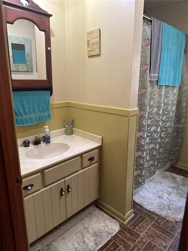 full bathroom featuring wainscoting, vanity, brick floor, and a shower with curtain