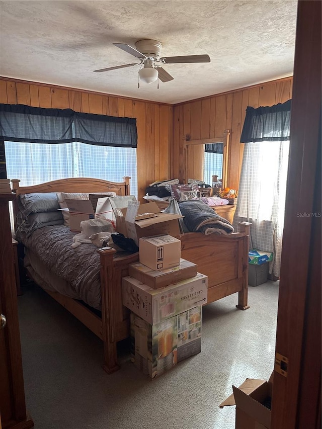 bedroom featuring carpet flooring, a ceiling fan, wood walls, and a textured ceiling