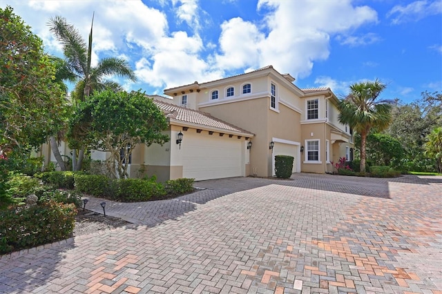 mediterranean / spanish home with a garage, decorative driveway, a tile roof, and stucco siding