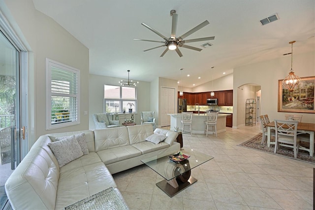 living area featuring light tile patterned floors, visible vents, arched walkways, vaulted ceiling, and ceiling fan with notable chandelier