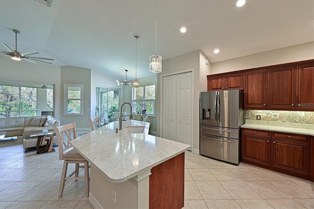 kitchen with a breakfast bar, a sink, hanging light fixtures, an island with sink, and stainless steel fridge