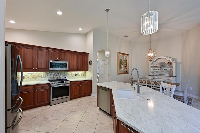 kitchen featuring light tile patterned floors, tasteful backsplash, appliances with stainless steel finishes, pendant lighting, and a sink