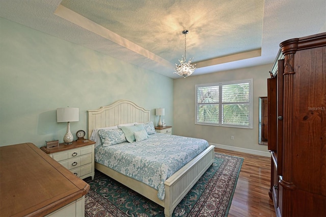 bedroom with a textured ceiling, a chandelier, wood finished floors, baseboards, and a tray ceiling