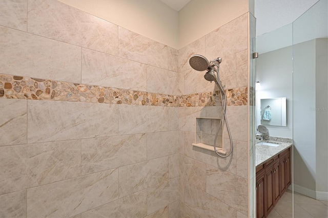 bathroom with tile patterned flooring, tiled shower, vanity, and baseboards