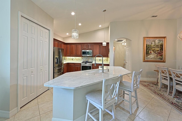 kitchen featuring light stone counters, arched walkways, pendant lighting, appliances with stainless steel finishes, and a sink