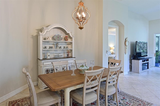 dining area featuring light tile patterned floors, a chandelier, arched walkways, and baseboards