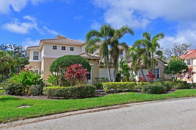 mediterranean / spanish house featuring a front yard, a tile roof, a residential view, and stucco siding