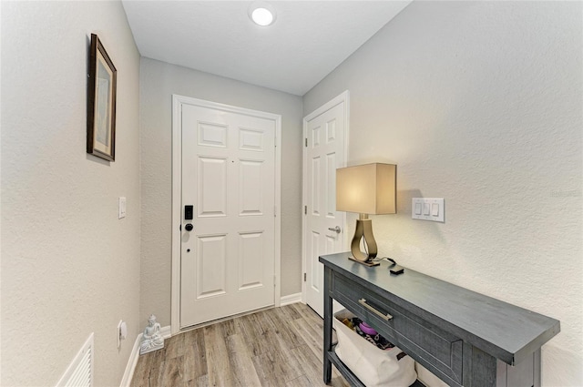 entryway featuring light wood finished floors, baseboards, visible vents, and a textured wall