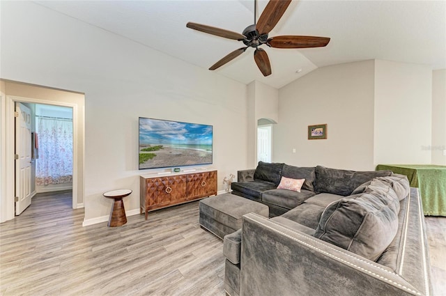 living area featuring arched walkways, high vaulted ceiling, light wood-style flooring, a ceiling fan, and baseboards