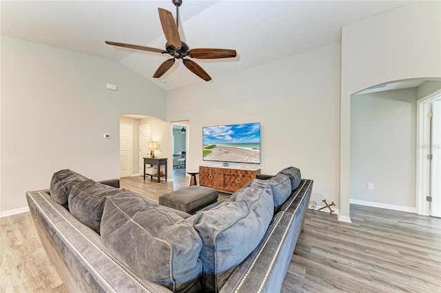 living room with light wood-type flooring, arched walkways, lofted ceiling, and baseboards