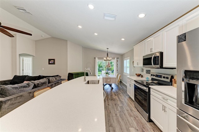 kitchen featuring white cabinets, appliances with stainless steel finishes, open floor plan, light countertops, and pendant lighting