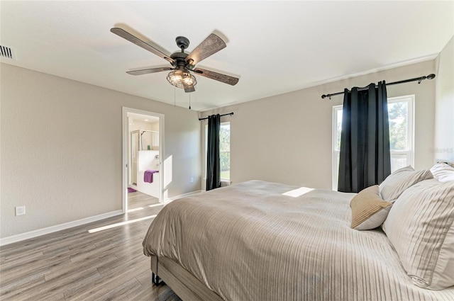 bedroom with visible vents, baseboards, a ceiling fan, ensuite bath, and wood finished floors