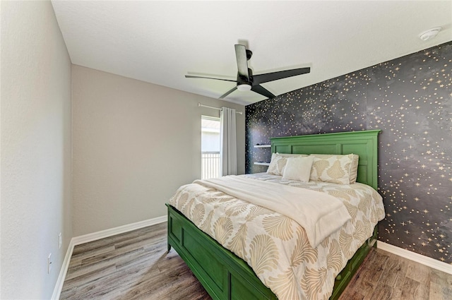 bedroom featuring an accent wall, wood finished floors, a ceiling fan, baseboards, and wallpapered walls