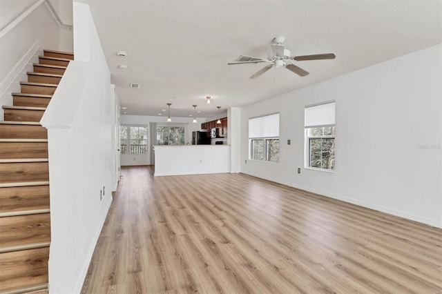 unfurnished living room featuring light wood finished floors, stairs, visible vents, and a wealth of natural light