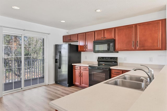 kitchen featuring light wood-style flooring, light countertops, black appliances, a sink, and recessed lighting