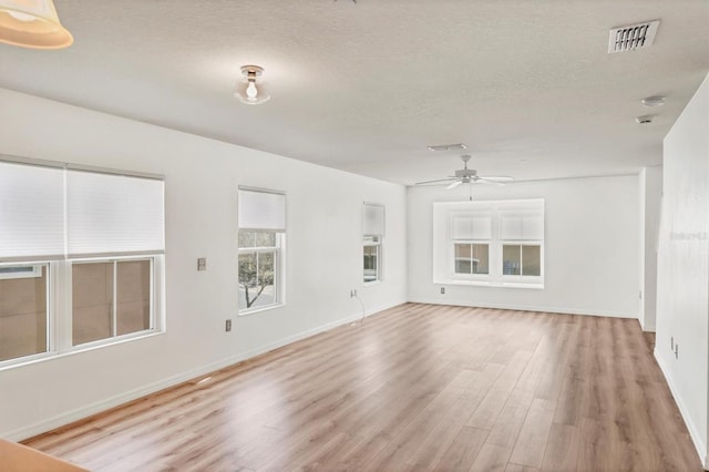 unfurnished living room featuring visible vents, light wood-style flooring, ceiling fan, a textured ceiling, and baseboards