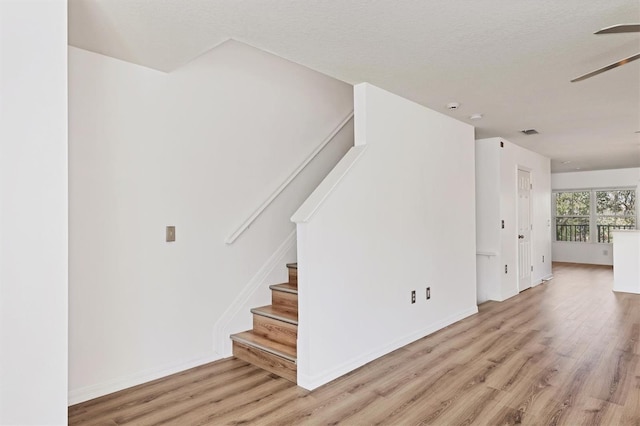 interior space with a textured ceiling, ceiling fan, wood finished floors, visible vents, and baseboards