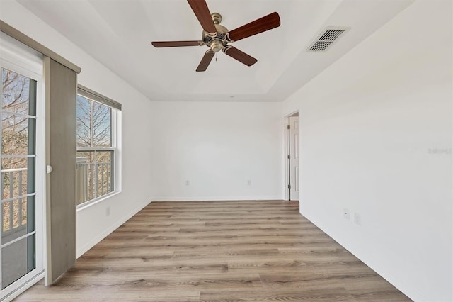 empty room with baseboards, visible vents, ceiling fan, a tray ceiling, and light wood-type flooring