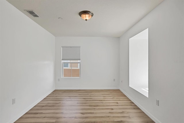 empty room with light wood-type flooring, visible vents, and baseboards