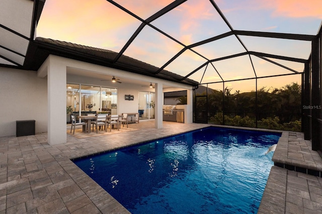 pool at dusk with a patio, exterior kitchen, a lanai, and an outdoor pool