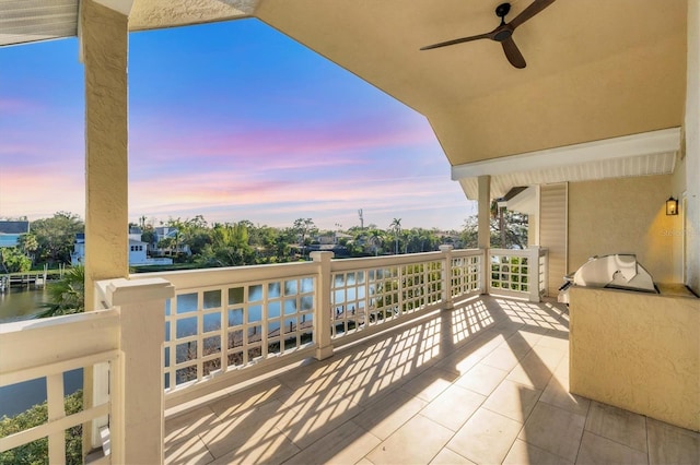 balcony at dusk with a water view and ceiling fan