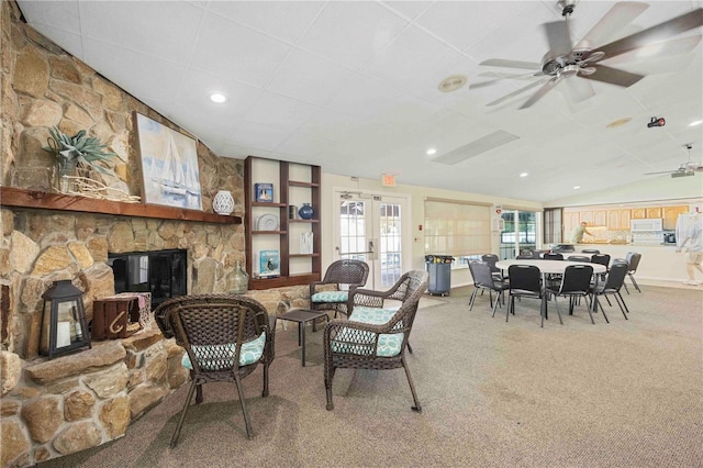 living room with carpet floors, a stone fireplace, a ceiling fan, and vaulted ceiling