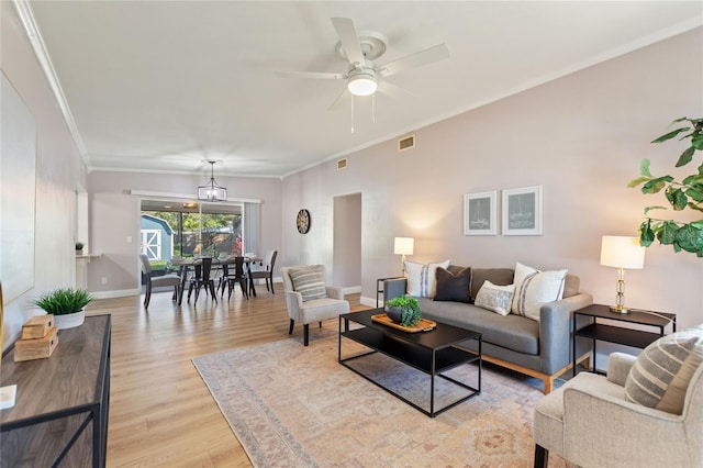 living room featuring light wood finished floors, visible vents, baseboards, crown molding, and ceiling fan with notable chandelier