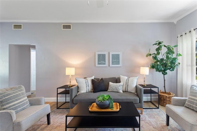 living area with crown molding, baseboards, visible vents, and light wood-style floors